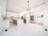 Gourmet kitchen featuring white shaker cabinetry, polished tile flooring, a large island with waterfall countertops, and integrated stainless steel ap