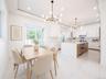 Open-concept kitchen and dining area featuring white cabinetry, a kitchen island with integrated appliances and wood-finish drawers, and sleek tile fl