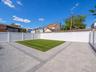 Expansive backyard featuring a manicured lawn, paver patio with a contrasting border, and white privacy fencing