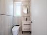 White floating vanity with a vessel sink, matte black faucet, and an illuminated oval mirror