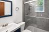 Bathroom featuring a vanity with an integrated sink, a toilet, a shower with a sliding glass door, grey tile surround, and a window