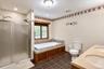 Dual vanity with integrated sinks, built-in Jacuzzi soaking tub, separate shower with frosted glass enclosure, and tiled flooring