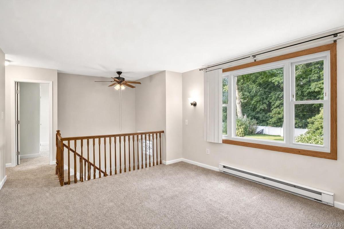 Carpeted interior with a large window, wooden railing, and a ceiling fan