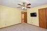 Ceiling fan with integrated lighting, wood-finish bi-fold closet doors, wall-mounted television, and neutral carpeting