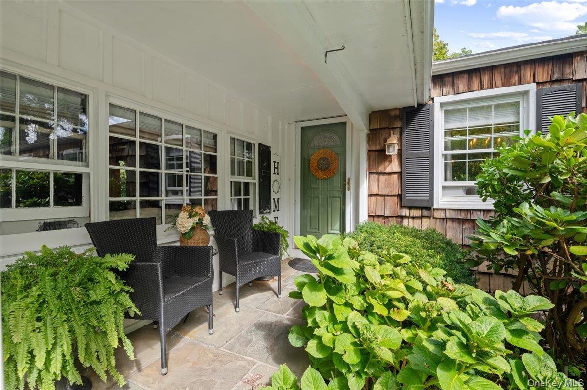 Stone patio with a covered entry, multiple multi-pane windows, and natural wood-shingle siding