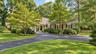 Asphalt driveway, manicured lawn, shaker siding, mature trees, and a covered entry