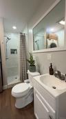Cottage full bathroom with wood-finish flooring, stacked laundry appliances, walk-in shower with glass enclosure, recessed lighting, and a vanity with