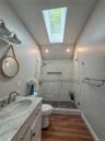 Cottage full bathroom with double vanity w/skylight feature, walk-in shower with glass enclosure and wood-finish flooring