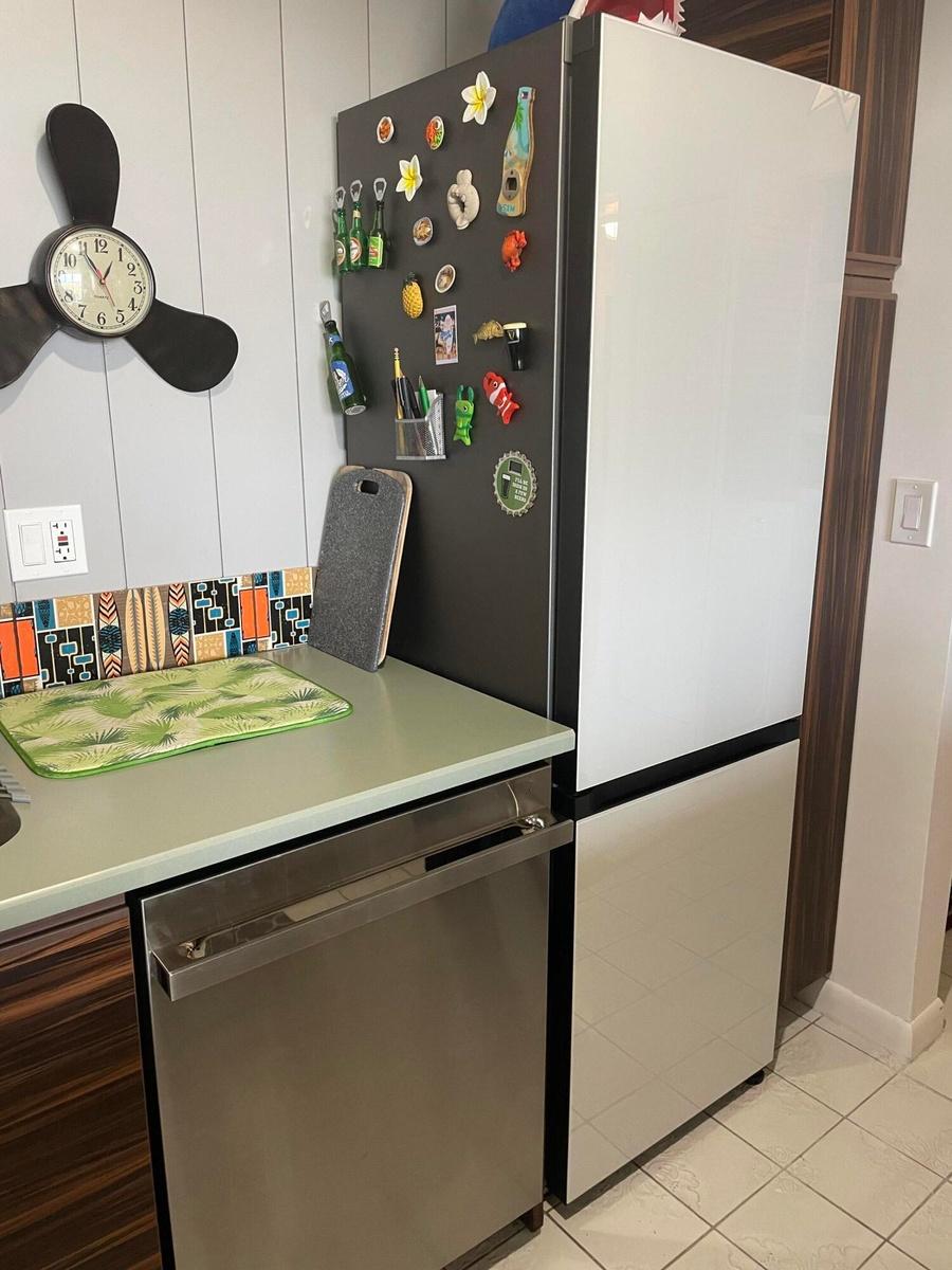 Stainless steel dishwasher, light green countertop, vertical plank wall paneling, and an integrated refrigerator