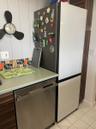 Stainless steel dishwasher, light green countertop, vertical plank wall paneling, and an integrated refrigerator