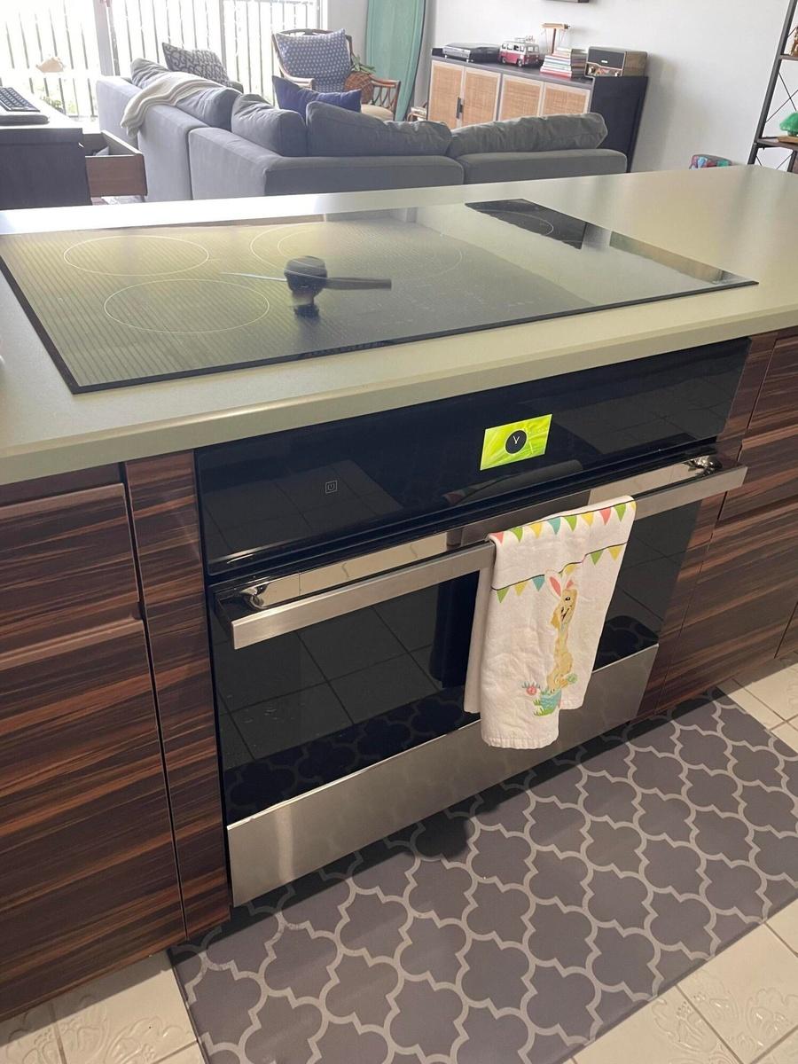 Built-in cooktop, integrated oven, wood-finish cabinetry, light-toned countertop, and tile flooring