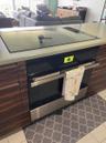 Built-in cooktop, integrated oven, wood-finish cabinetry, light-toned countertop, and tile flooring