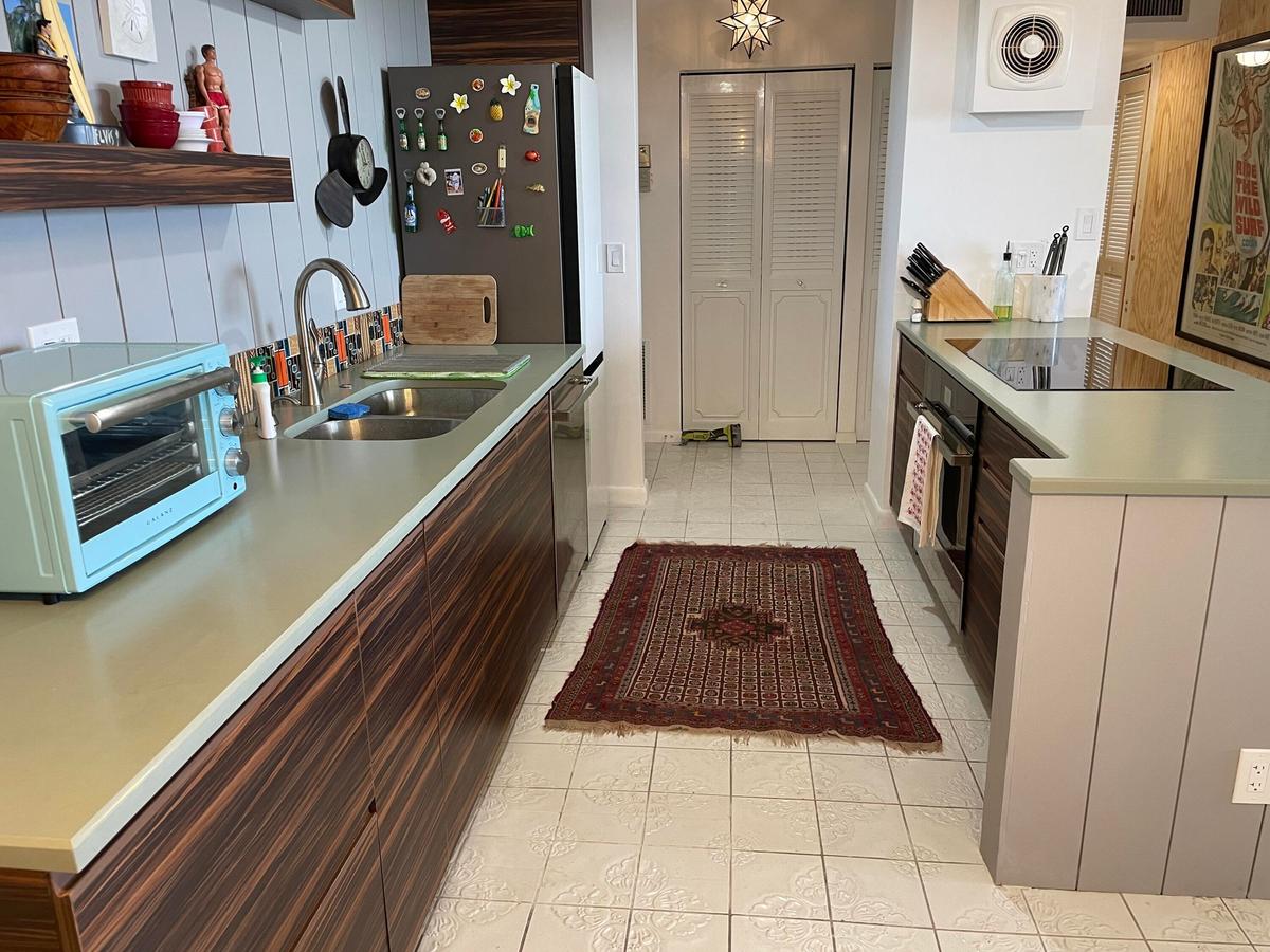 Galley kitchen featuring wood-finish cabinetry, light-toned countertops, a stainless steel sink with a gooseneck faucet, an integrated cooktop, and ti