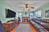 Hardwood flooring complemented by a stone-faced wood burning fireplace, a ceiling fan with integrated lighting, and multiple windows