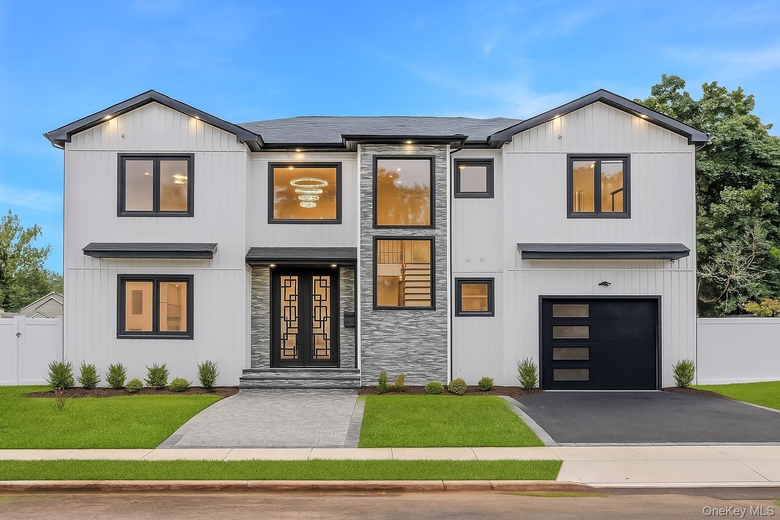 Contemporary exterior featuring white vertical siding, black-framed windows, a two-car garage with a modern door, a stone-clad entry, and a paved walk