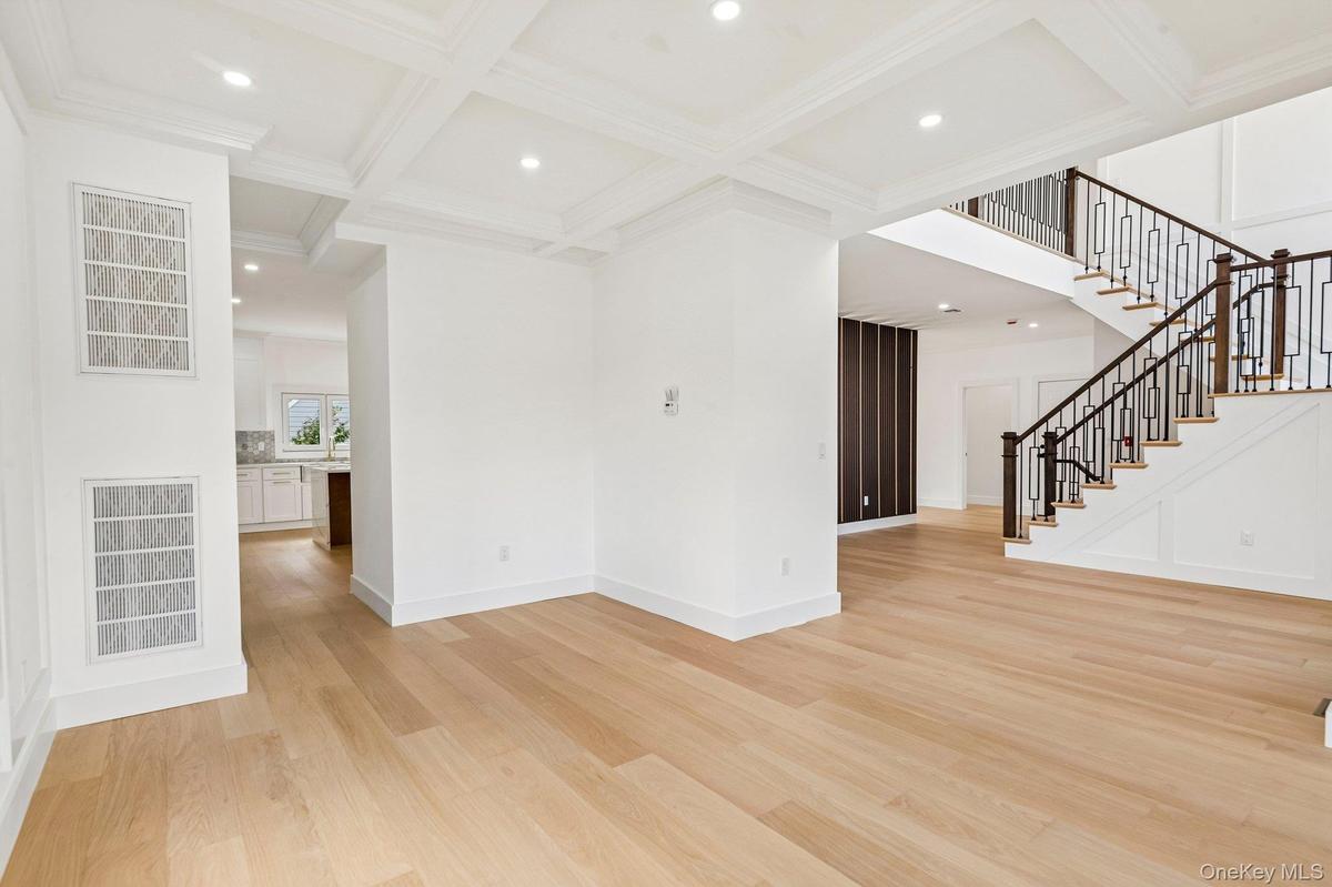 Light wood-finish flooring, coffered ceiling with recessed lighting, and a staircase featuring dark wood handrails with decorative metal balusters