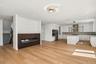 Light wood-finish flooring, built-in electric fireplace with slatted paneling, white shaker cabinetry, stainless steel appliances, and a kitchen islan