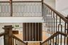 Wood-finish staircase with black metal balusters, hardwood flooring, and a decorative slatted wall panel