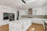 Gourmet kitchen featuring a waterfall island, stainless steel appliances, honeycomb tile backsplash, white cabinetry with gold-tone hardware, and wood