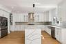 Gourmet kitchen featuring white shaker cabinetry, stainless steel appliances, a waterfall island, hexagon tile backsplash, and wood-finish flooring