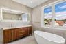 Freestanding soaking tub, dual-pane windows, wood-finish double vanity with stone countertop, and an illuminated mirror