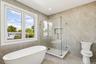 Freestanding soaking tub, glass-enclosed shower with built-in bench, recessed shower niche, contemporary wall tiles, and large window with white trim