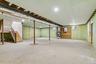Spacious unfinished lower level with concrete flooring, recessed lighting, exposed ceiling joists, and a finished wooden staircase with railing