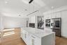 Kitchen island with waterfall countertop, stainless steel appliances, white cabinetry with gold-tone hardware, light wood-finish flooring, and recesse