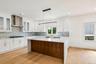 White shaker cabinetry with gold-tone hardware, hexagonal tile backsplash, stainless steel range hood, integrated kitchen island with contrasting wood