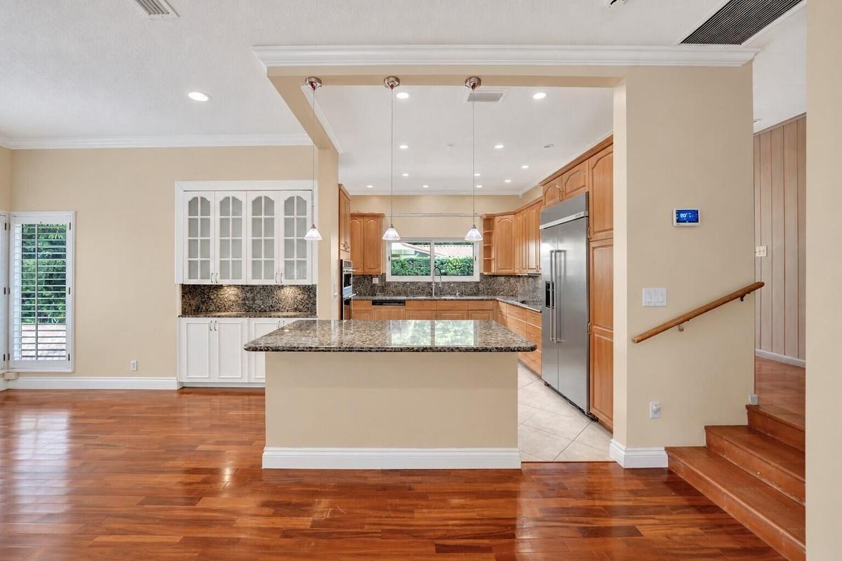 Wood-finish flooring throughout, kitchen with wood cabinetry and stainless steel appliances, breakfast bar with stone countertop, white built-in cabin