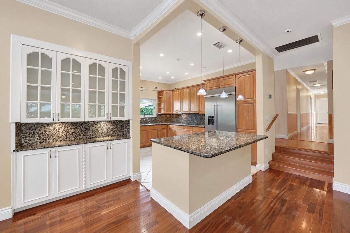 Wood flooring throughout, with a built-in white cabinetry unit featuring glass panel doors and under-cabinet lighting. Wall color has been virtually e