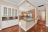 Wood flooring throughout, with a built-in white cabinetry unit featuring glass panel doors and under-cabinet lighting. Wall color has been virtually e