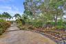 Expansive flagstone patio with a stone retaining wall, varied landscaping, and mature trees