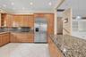 Kitchen featuring extensive wood cabinetry, stainless steel refrigerator, patterned stone countertops, recessed lighting, and tile flooring. Wall colo