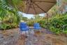 Stone patio with alcove sitting areas, an umbrella shade and lush tropical landscaping