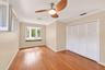 Hardwood flooring, bay window with integrated seating, white louvered bifold closet doors, crown molding, and ceiling fan with integrated lighting