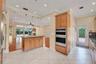 Kitchen featuring an island with granite countertops, built-in double ovens, light wood cabinetry, and recessed lighting. Wall color has been virtuall