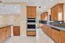 Kitchen featuring wood cabinetry, stainless steel double wall oven, neutral tile flooring, and dark speckled countertops. Wall color has been virtuall