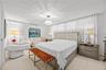 Spacious primary bedroom with room to relax, featuring a sitting nook, air conditioning, and soft natural light through sheer drapery