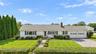 White ranch-style residence featuring a two-car garage, brick chimney, established front landscaping, and a paved driveway