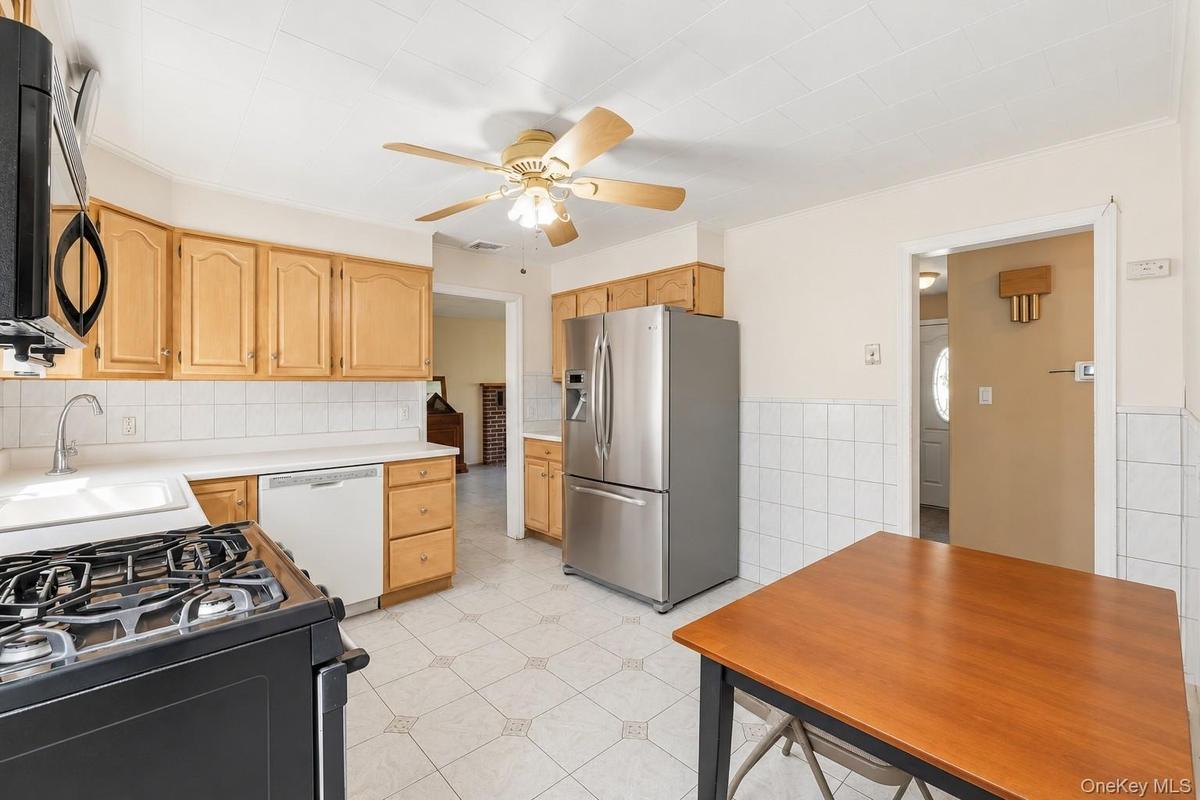 **Virtually Staged** Kitchen featuring wood-finish cabinetry, stainless steel refrigerator, white tile backsplash, and a ceiling fan with integrated l