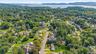 Aerial view showcasing a tree-lined residential community with mature landscaping, spacious home lots, and a serene waterfront backdrop