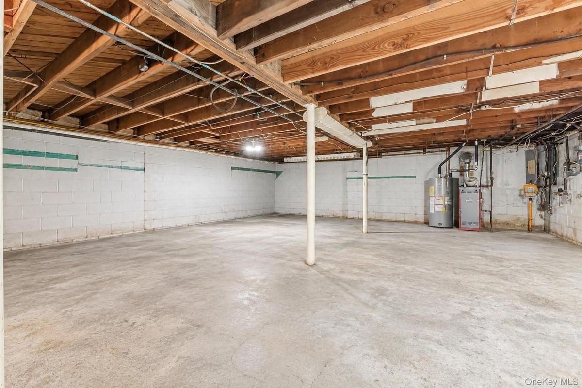Expansive unfinished basement featuring a concrete floor, exposed wood beams, and painted block walls
