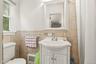 White pedestal sink with chrome faucet, framed mirror, and tiled walls