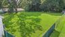 Expansive grassy yard featuring a chain-link fence, mature trees, and a shaded area