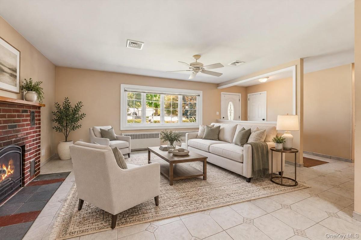 **Virtually Staged** Sophisticated living room featuring a working fireplace with brick surround, large multi-pane windows with natural light, ceiling