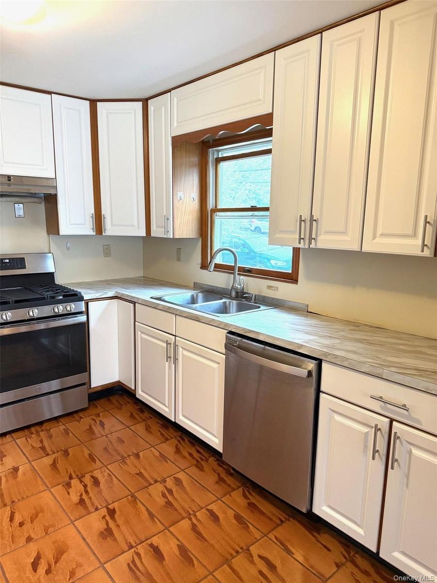 Kitchen featuring white cabinets, stainless steel appliances, light countertops, and dark tile patterned floors