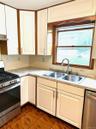Kitchen featuring stainless steel appliances, white cabinets, light countertops, dark tile patterned floors, and under cabinet range hood