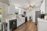 Kitchen featuring white shaker cabinetry, white quartz countertops, a decorative tile backsplash, stainless steel appliances, and wood-finish flooring