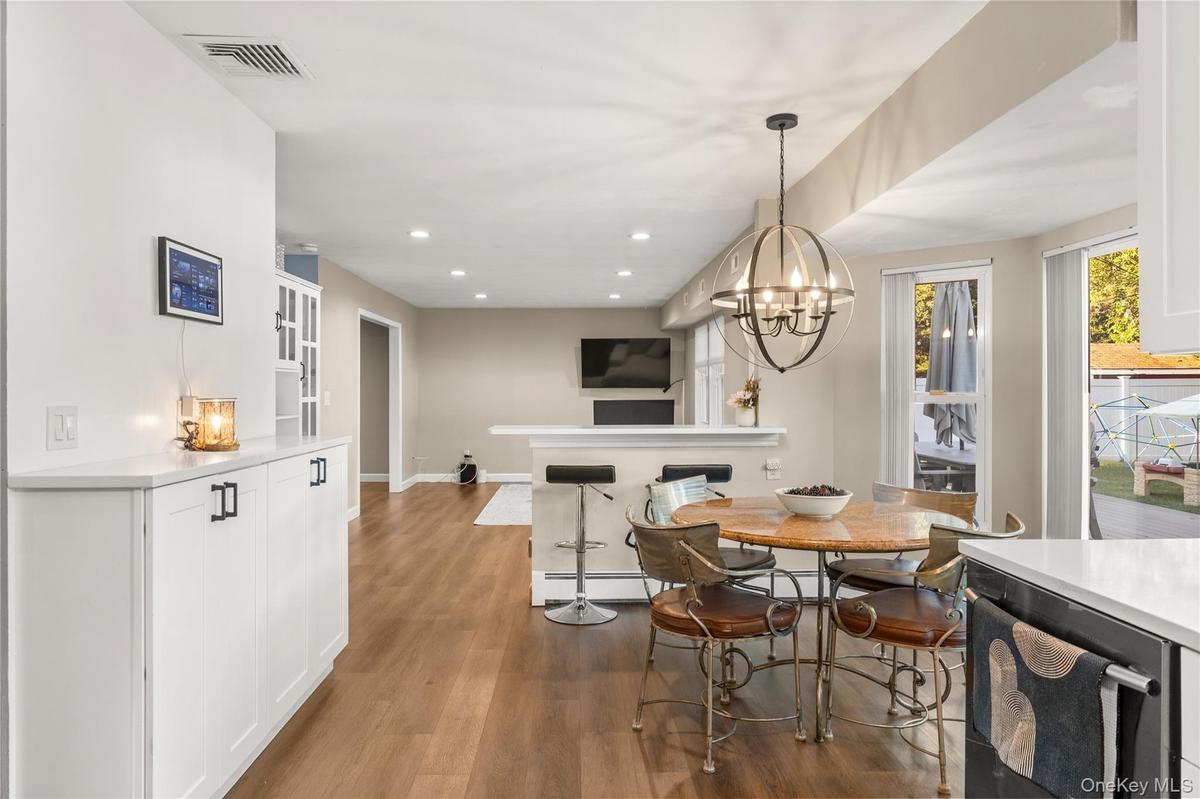 Eat in kitchen area with bar height seating. Wood-finish flooring throughout, recessed lighting, and a modern globe chandelier. Built in white cabinet